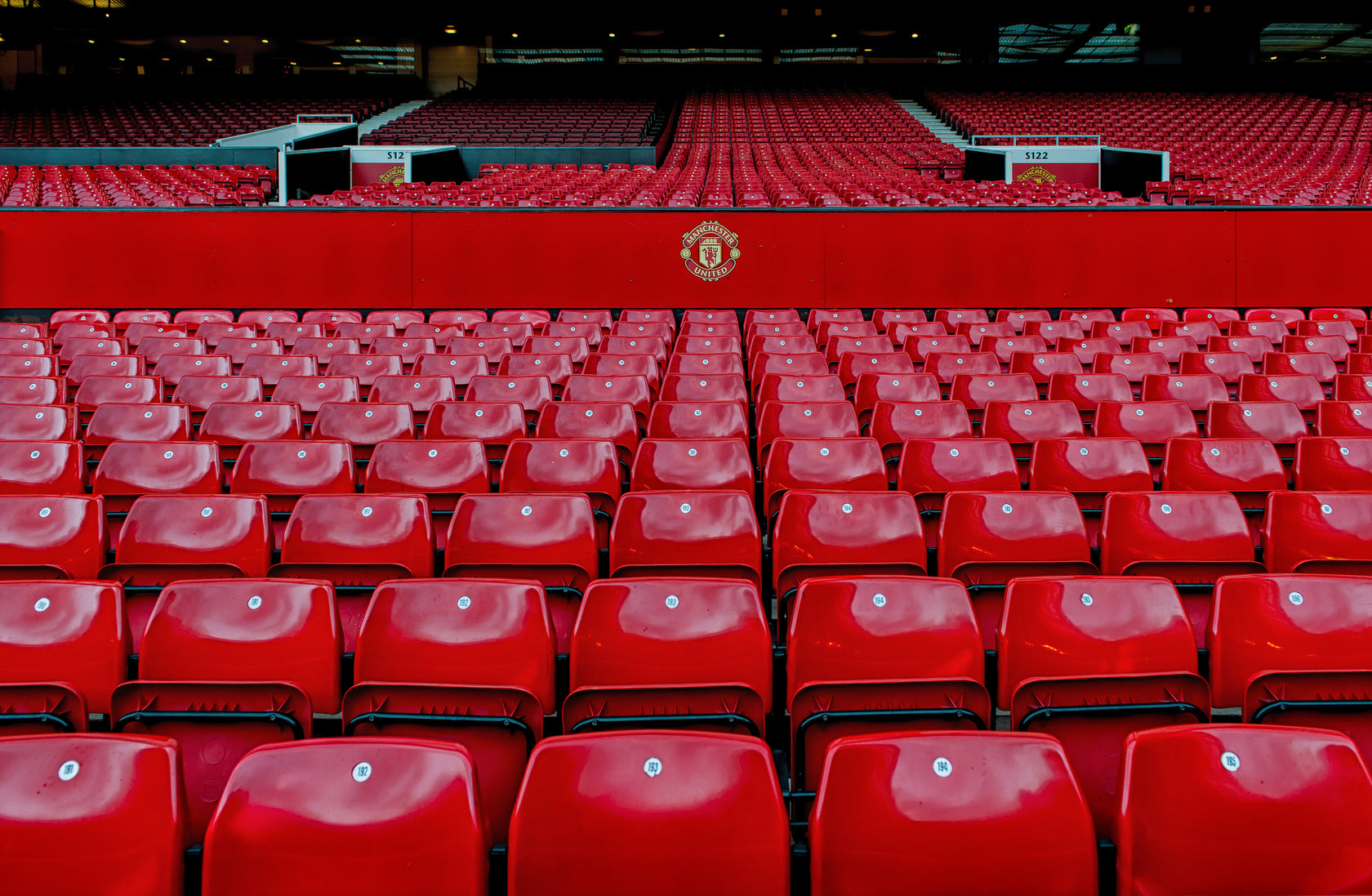wideshot of rows of bright red seats with the Manchester United logo halfway up the stand
